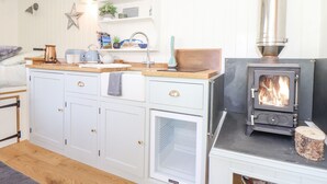 A cozy kitchen with a wood-burning stove, a built-in sink, and a small island with a kettle. - Gwithian Shepherds Hut (Hayle)
