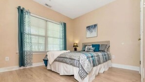 A bedroom with a bed, a nightstand, a window with curtains, and a painting on the wall.