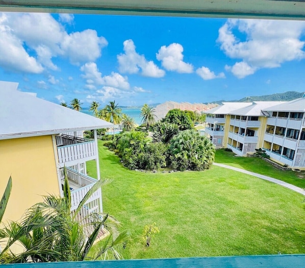 A hotel with a pool, surrounded by lush greenery and a view of the ocean.