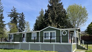 A single-story mobile home with a covered porch and a fenced yard. - Encanto's House – A Forest Haven (Marysville)