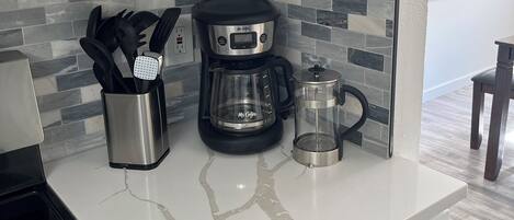 Une cuisine avec des meubles blancs, une machine à café, un moulin à café et une bouilloire, le tout posé sur un plan de travail en marbre.