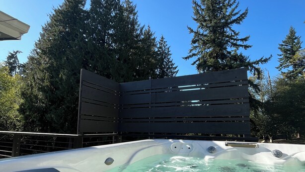 A hot tub with clear water, surrounded by a metal fence and tall trees. - Encanto's House – A Forest Haven (Marysville)