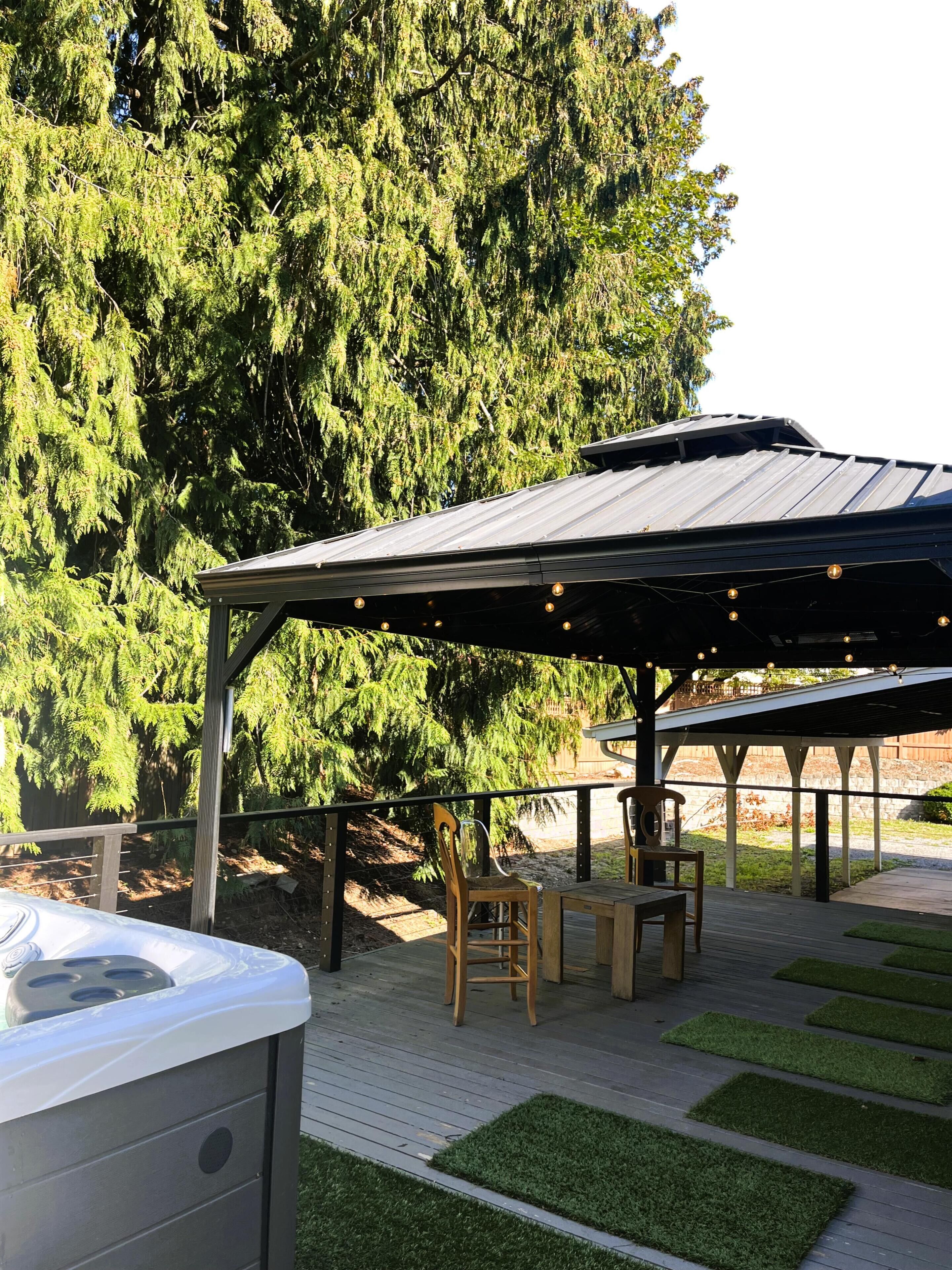 Un patio esterno coperto con vasca idromassaggio, sedie di legno e un tavolo.