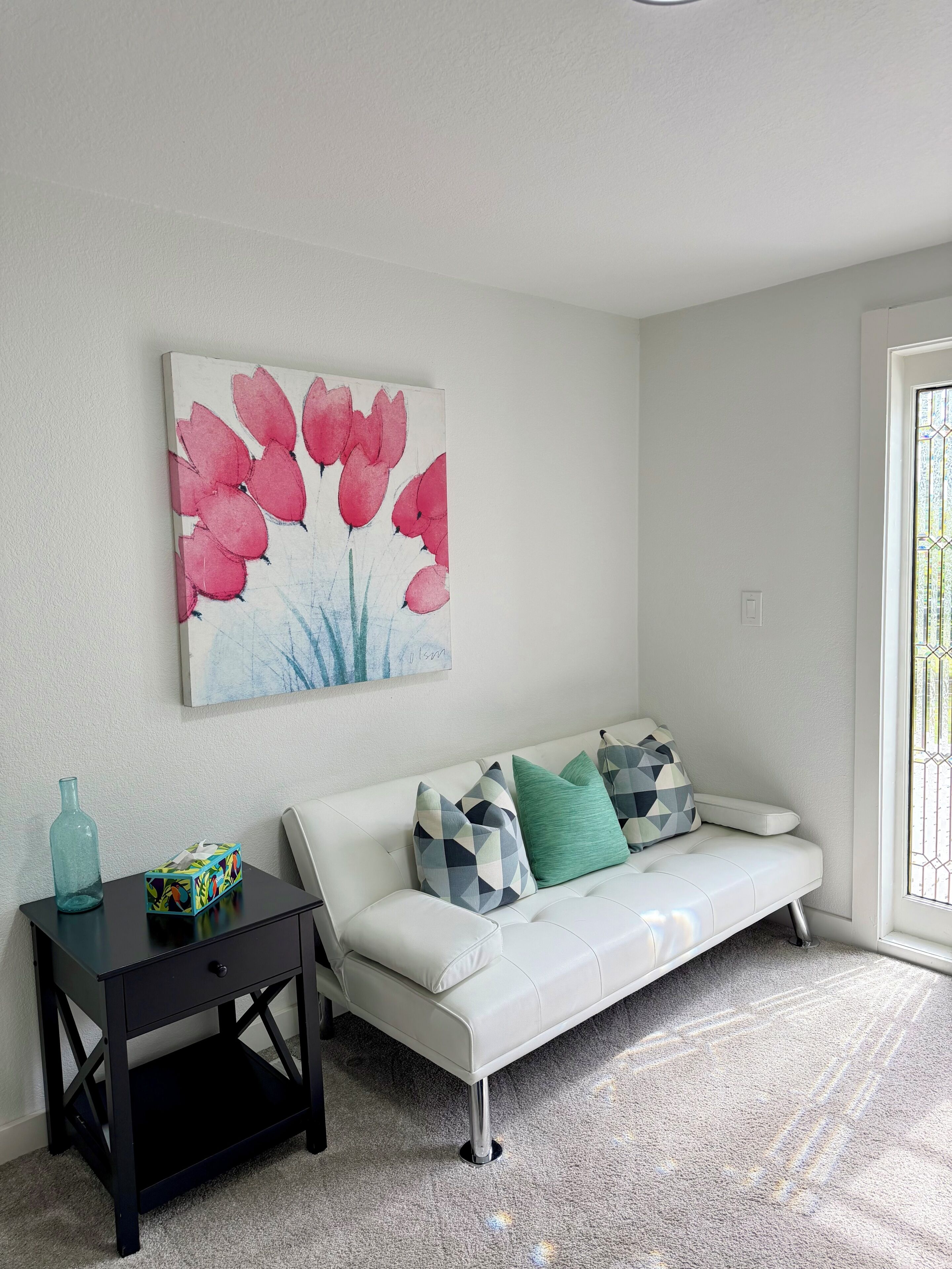 A living room with a white sofa, a black side table, and a colorful abstract painting.