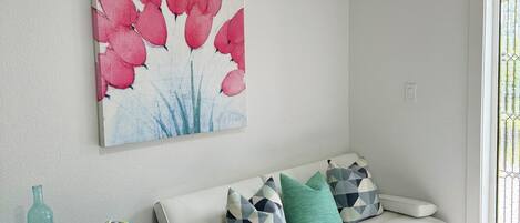 A living room with a white sofa, a black side table, and a colorful abstract painting.