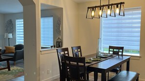 A dining area with a wooden table and chairs, a chandelier, and a view through the window. - Encanto's House – A Forest Haven (Marysville)