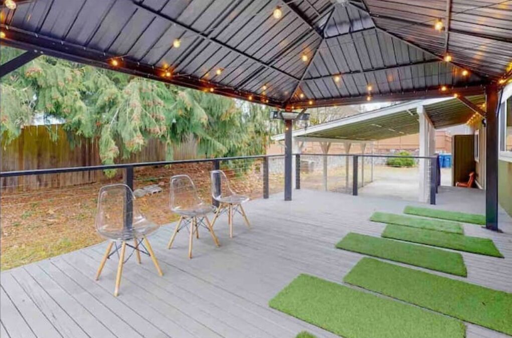 A covered outdoor area with a wooden deck, clear chairs, and green mats.