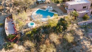 Vue aérienne d’une propriété dotée d’une piscine, d’une terrasse aménagée avec des sièges et d’un bâtiment à la façade rose.