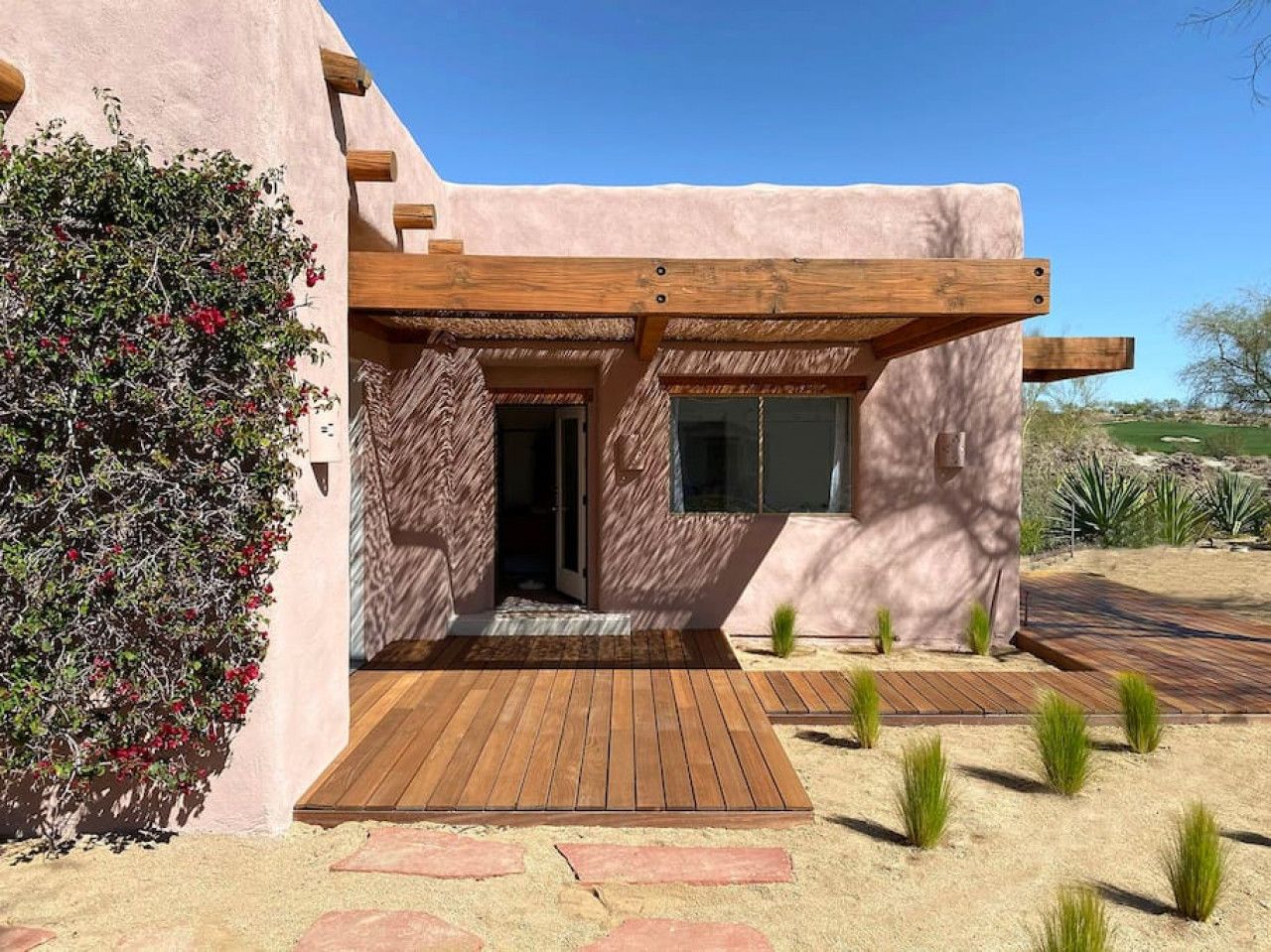 A modern building with a wooden deck, a covered entrance, and a desert garden.