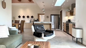 A modern living room with a leather chair, a sofa, and a coffee table. There is a kitchen area with a refrigerator, oven, and sink. - Mediterranean-modern estate with breathtaking views that sleeps 12 (Palm Desert)