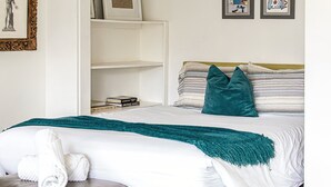 A neatly made bed with a teal throw blanket, a pillow, and a rolled towel on a leather ottoman. - The Peach Residence (Palm Springs)