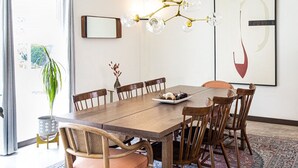 A dining area with a wooden table and chairs, a chandelier, and a large abstract painting on the wall. - The Peach Residence (Palm Springs)