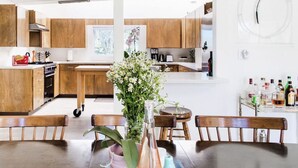 A modern kitchen with wooden cabinets, a dining table with chairs, and a vase of flowers. - The Peach Residence (Palm Springs)