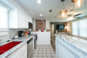 A modern kitchen with white cabinets, a red sink, patterned floor tiles, and a central island with a decorative panel.