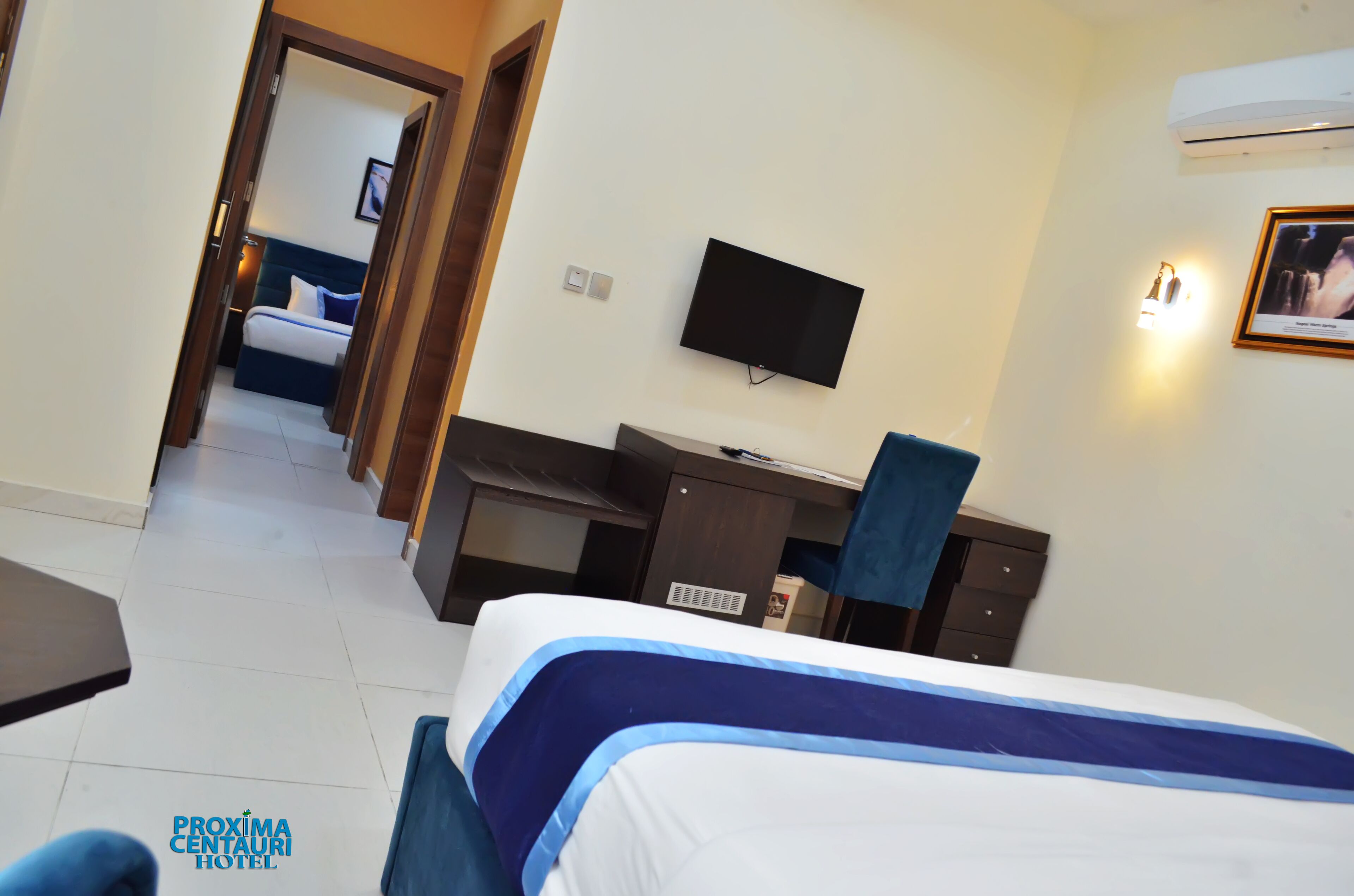 A hotel room with a bed, a desk, a chair, a television, and a wall-mounted air conditioner.