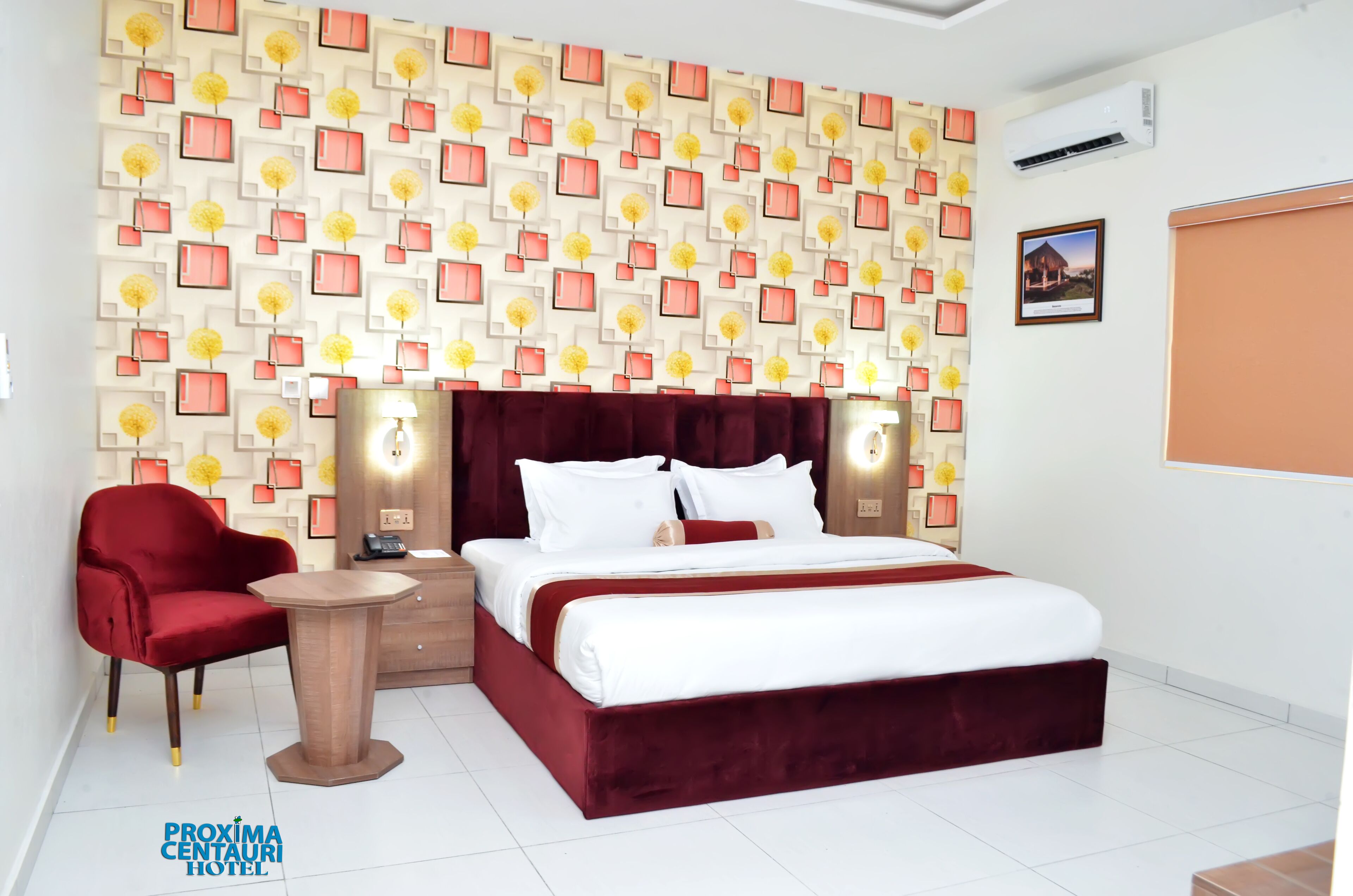 Une chambre d’hôtel avec un lit recouvert de velours rouge, un fauteuil rouge, une petite table en bois et un mur orné d’un motif.