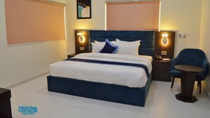 Une chambre d’hôtel avec un grand lit, des tables de chevet, une chaise et une lampe fixée au mur.
