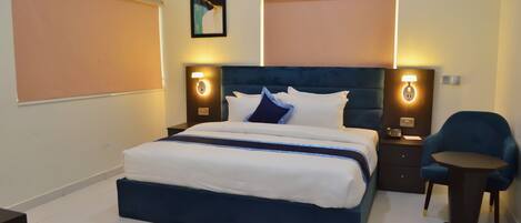 Una habitación de hotel con una cama grande, mesitas de noche, una silla y una lámpara fijada a la pared.