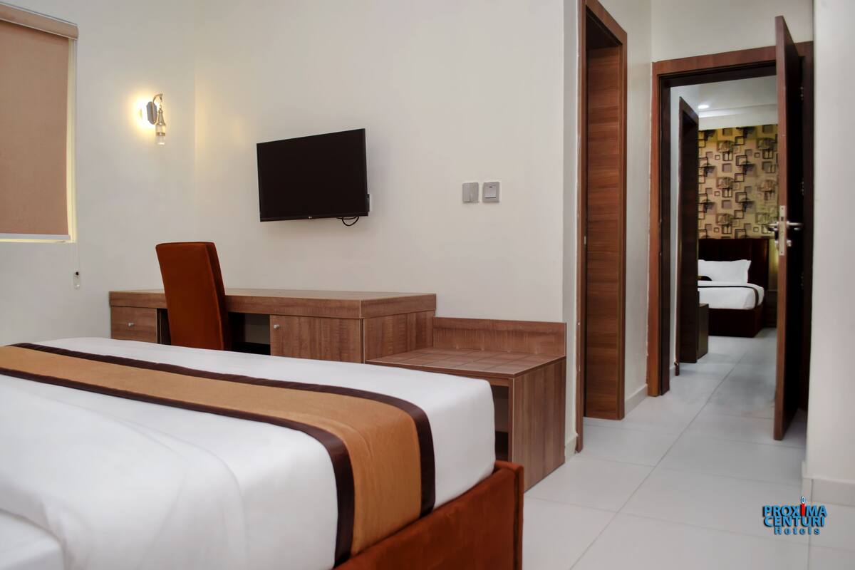 Habitación de hotel con cama, escritorio, silla, televisión y baño visible a través de una puerta abierta.