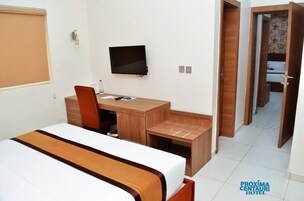 Una habitación de hotel con cama, escritorio, silla, televisor y armario.