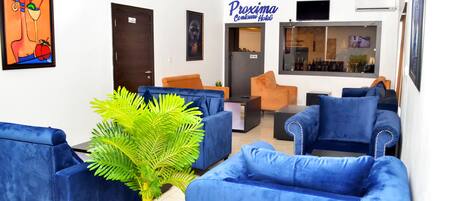 A hotel lobby with blue sofas, a large potted plant, and a sign for 'Proxima Contini Hotel'.