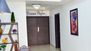 Un intérieur moderne avec un escalier menant à une porte en bois sombre portant l’inscription « Cuisine Centauri ». Un tableau noir avec le menu est visible sur le mur, et une œuvre d’art encadrée est accrochée au-dessus de la porte.