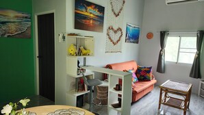 A living room with a sofa, a small table, a decorative wall hanging, and a window with curtains. - Coastal house near the beach, AC, peaceful, great location, outdoor restaurant. (Salak Phet)