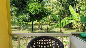 A balcony with a glass table and two chairs, overlooking a lush garden with various trees and plants. - Coastal house near the beach, AC, peaceful, great location, outdoor restaurant. (Salak Phet)