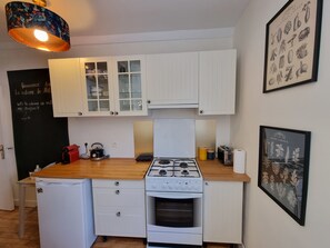 Cozinha compacta com armários brancos, fogão a gás, forno embutido, cafeteira e quadro negro com anotações.