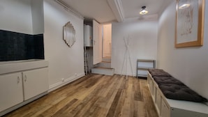 A modern kitchen with white cabinets, a black backsplash, and wooden flooring. There is a bench with a cushion in the corner and a ladder leaning against the wall.
