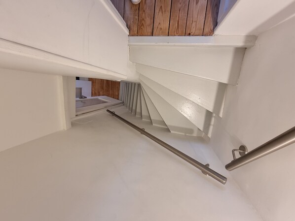 A white staircase with a wooden finish at the top, leading to a lower level.