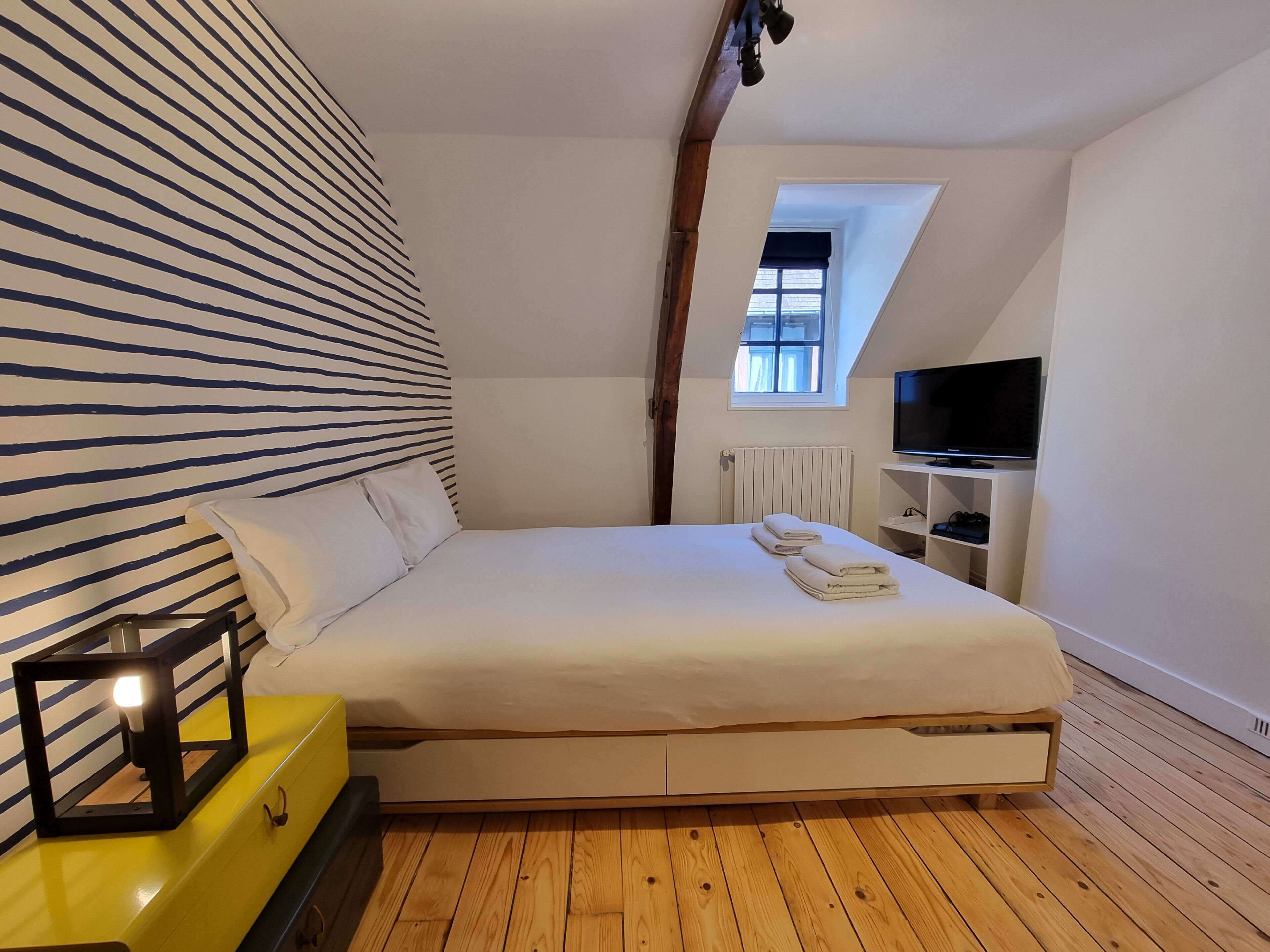 Une chambre à coucher avec un lit, une télévision, une fenêtre et un plancher en bois.