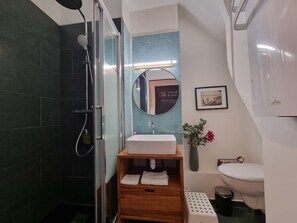 Un baño moderno con cabina de ducha de vidrio, tocador de madera con lavamanos, inodoro y espejo con un cuadro enmarcado.