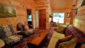 Ein gemütliches Blockhaus-Interieur mit einer Couch, zwei gemusterten Sessel, einem Holztisch und einem Teppich.