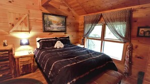 Ein gemütliches Schlafzimmer in einer Holzhütte mit Bett, Nachttisch, Lampe und einem Fenster mit Vorhängen.