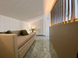 Ένα μοντέρνο σαλόνι με έναν μπεζ καναπέ, ένα μικρό τραπεζάκι με ένα φωτιστικό και ένα καλοριφέρ.