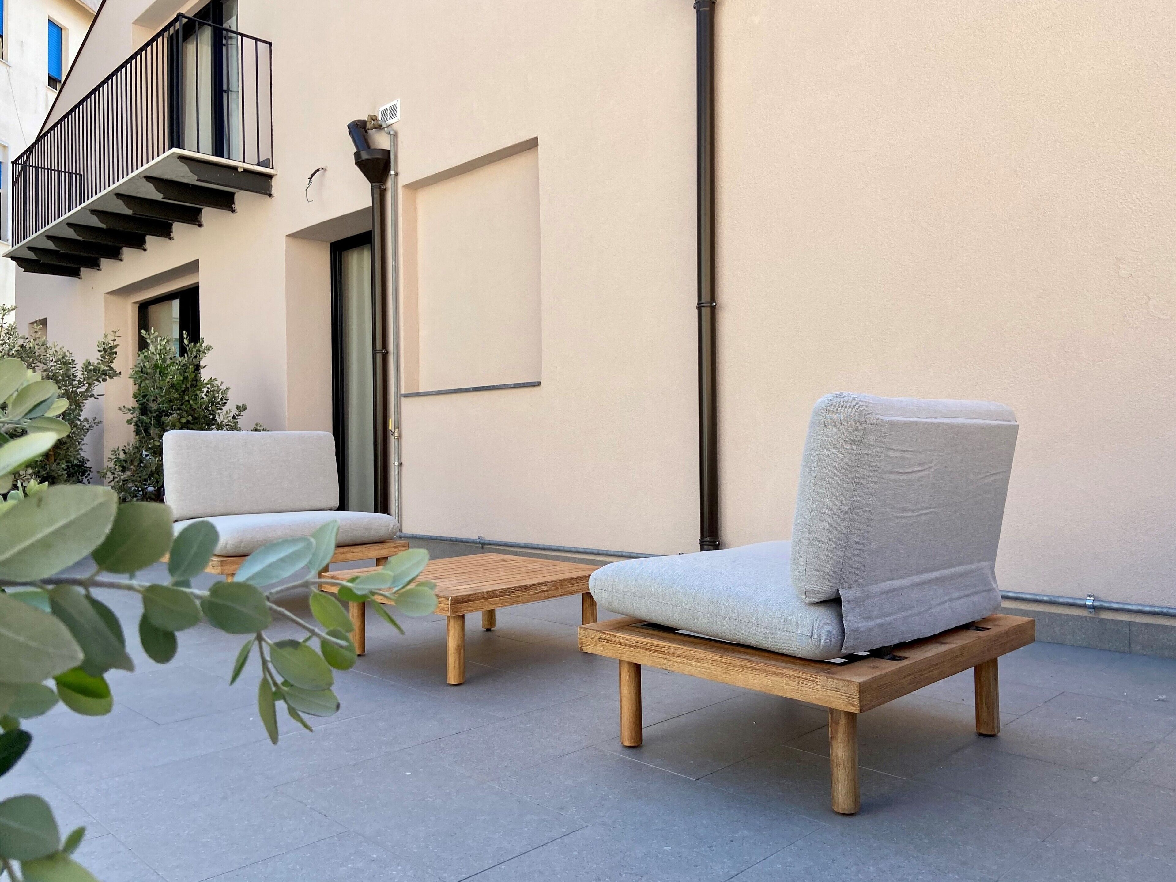 Een terras met twee houten stoelen en een kleine tafel, een trap en een gevel.