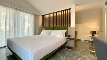 A modern hotel room with a large bed, a nightstand, a chair, and a view of the city through large windows.