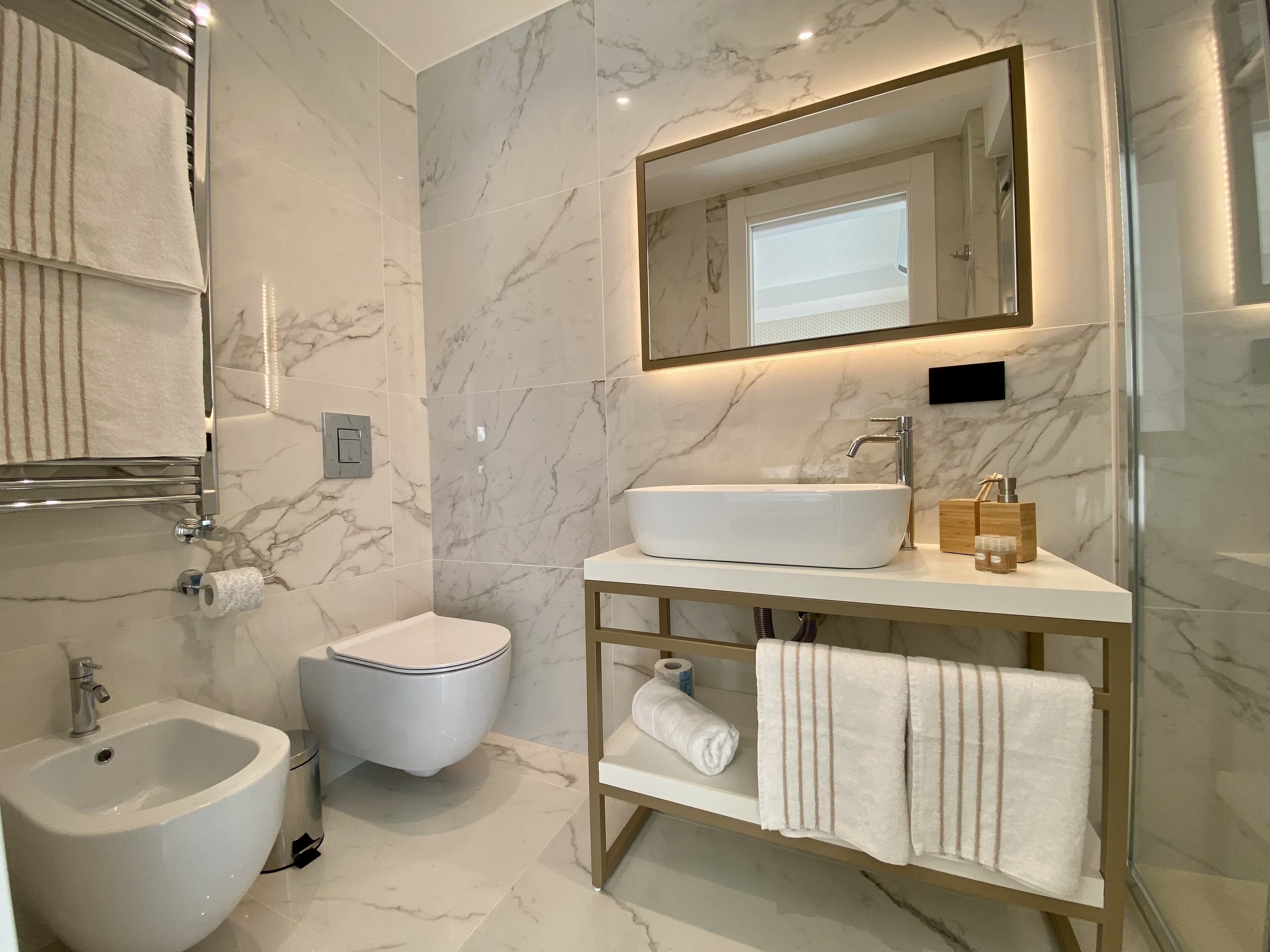 A modern bathroom with a white sink, a bidet, a toilet, and a vanity with a mirror.