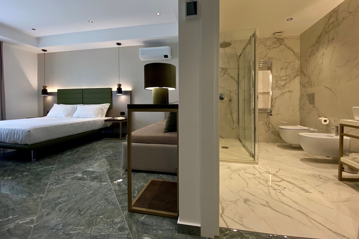 Ein modernes Hotelzimmer mit Bett, Sitzecke, Dusche und Marmorböden.