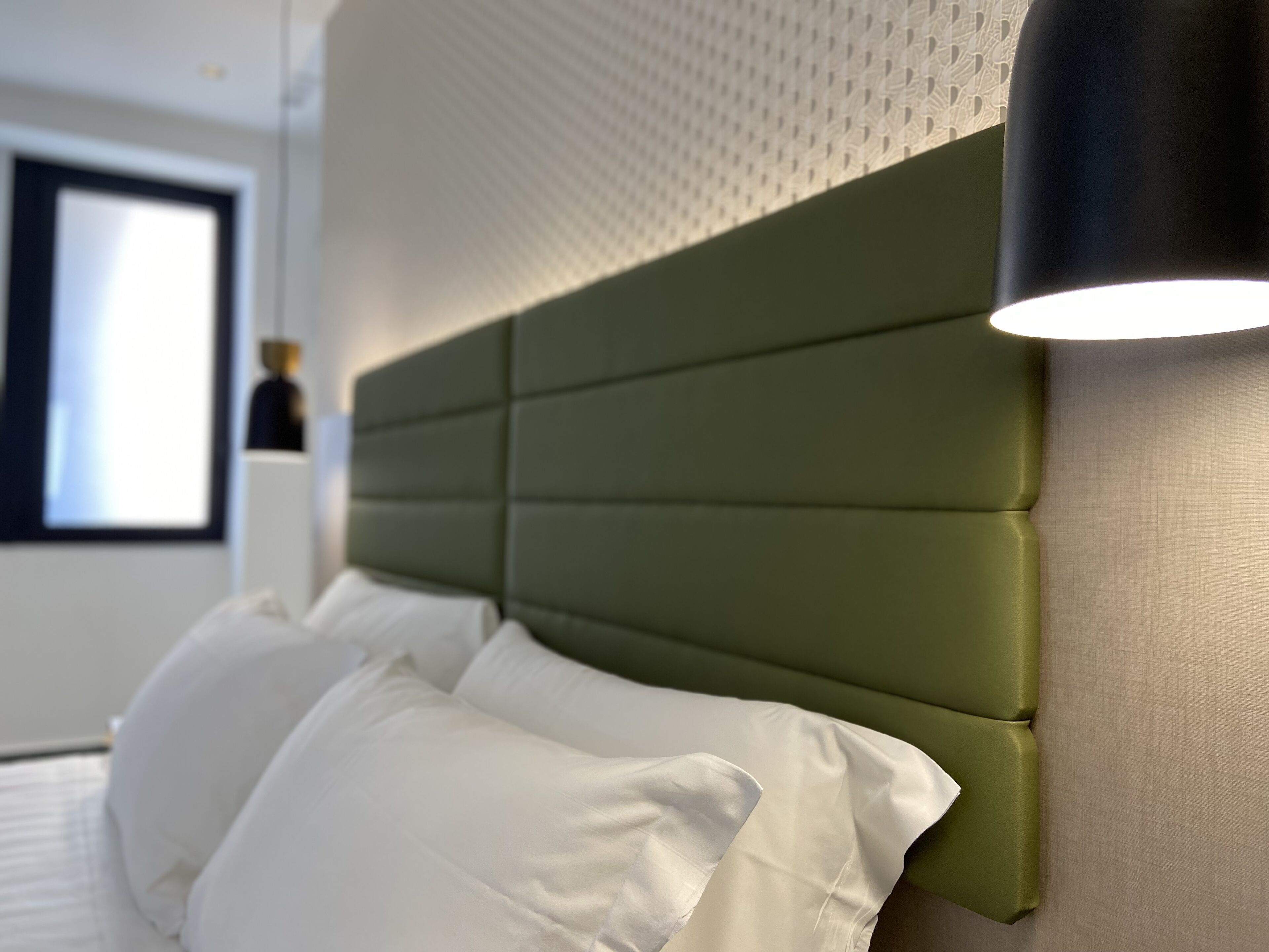 A bed with white pillows and a green upholstered headboard in a hotel room.