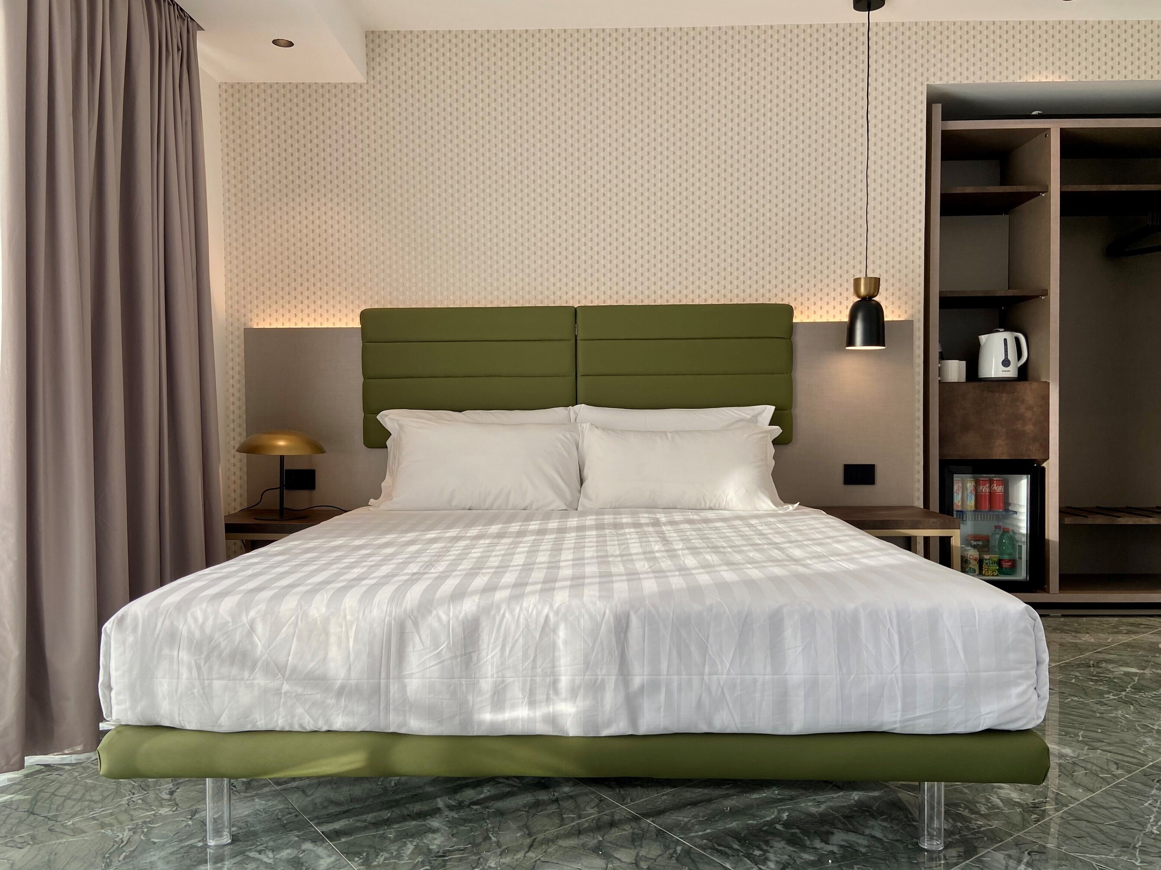 Una cama bien hecha con un cabecero verde, una mesita de noche con una lámpara, y un armario con espejo.