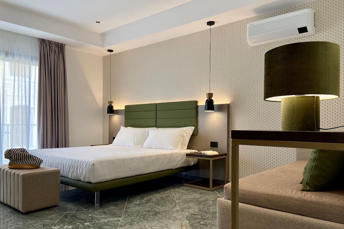 A modern hotel room with a large bed, a nightstand, a reading lamp, a chair, and a marble floor.