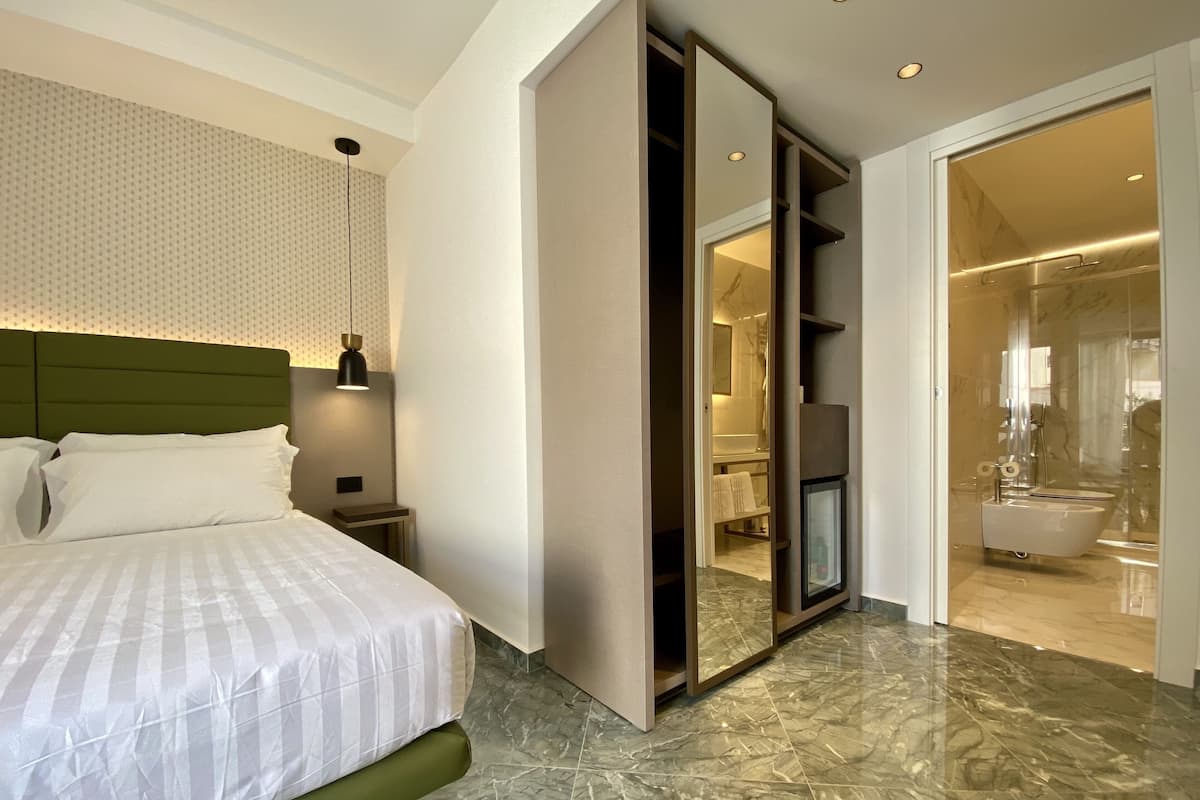 A modern bedroom with a bed, a nightstand, a mirror, and a bathroom with a shower and toilet.
