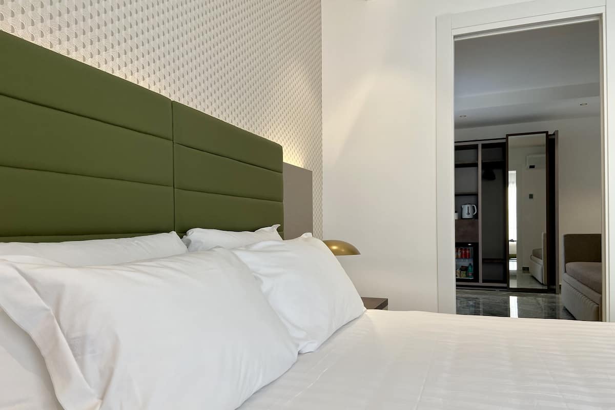 A neatly made bed with white linens and a green headboard in a hotel room.