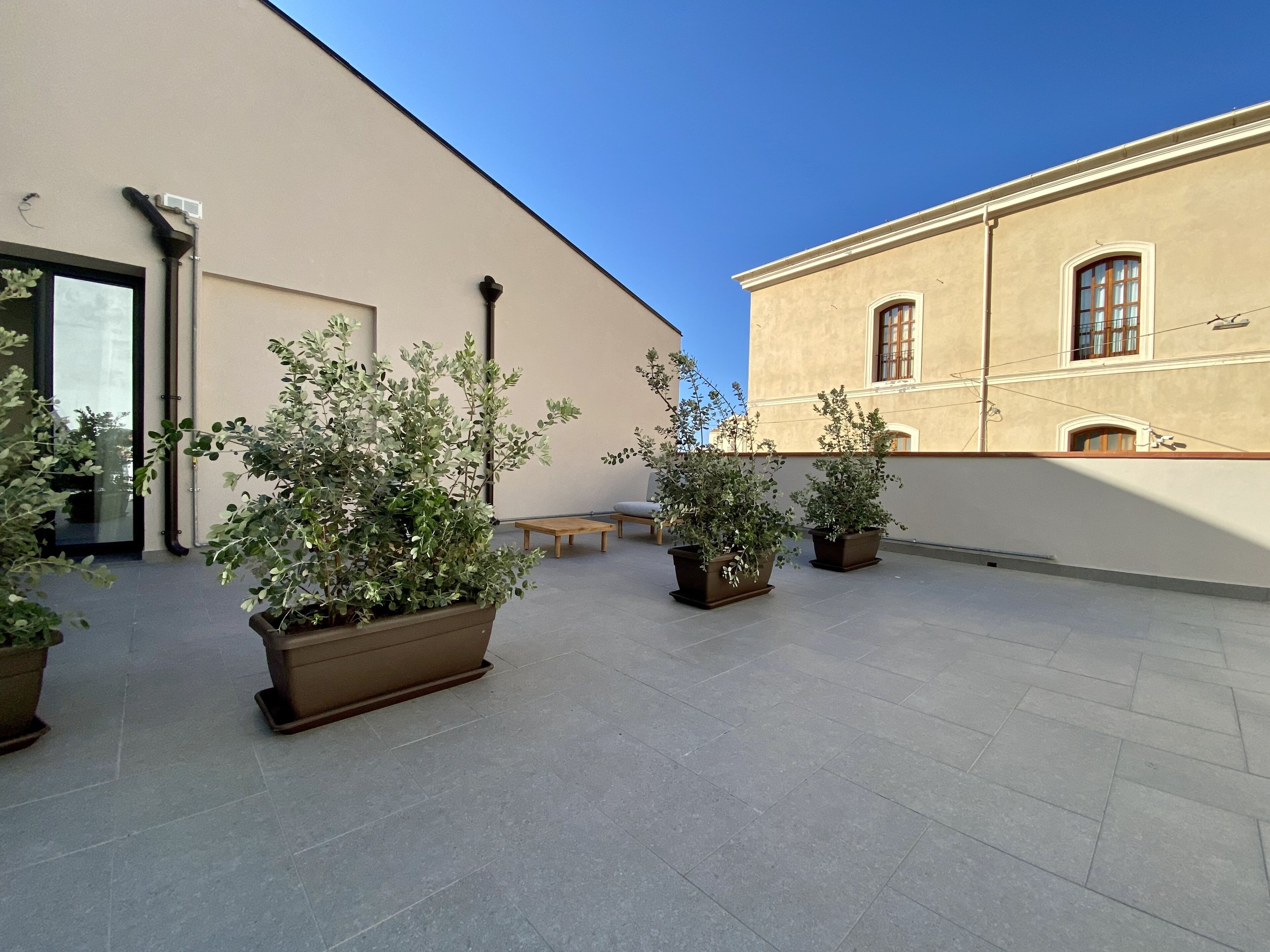 An outdoor patio area with potted plants, a bench, and a building facade.