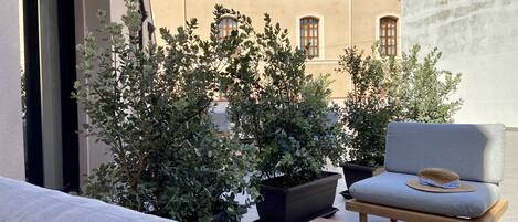 A patio with a sofa, a wooden table, and potted plants.