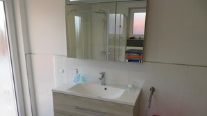Une salle de bain avec un lavabo, un miroir et une poubelle rose.