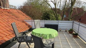 Une terrasse sur le toit avec une table verte et deux chaises, un barbecue et des plantes en pot.