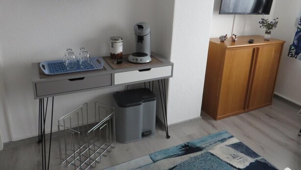 Un espace de vie compact comprenant un coin cuisine, un téléviseur fixé au mur et un petit meuble de rangement.